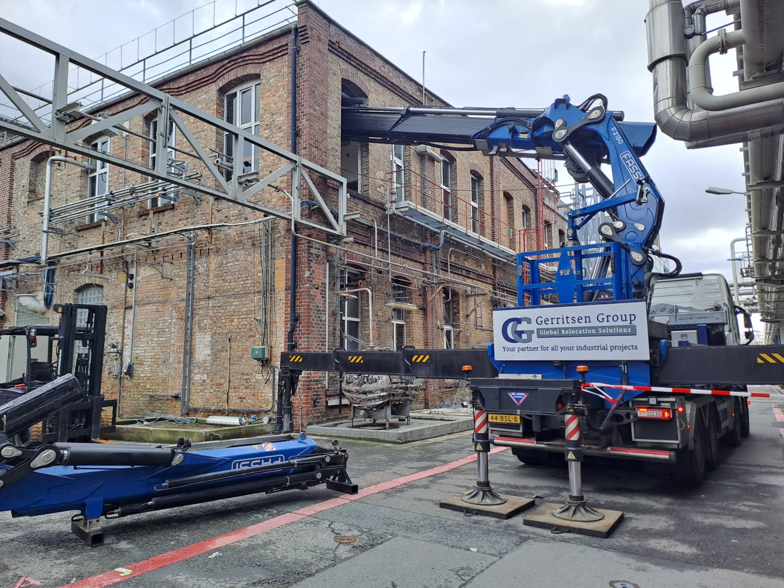 Truck mounted crane operating through a window of a building on a plant. 