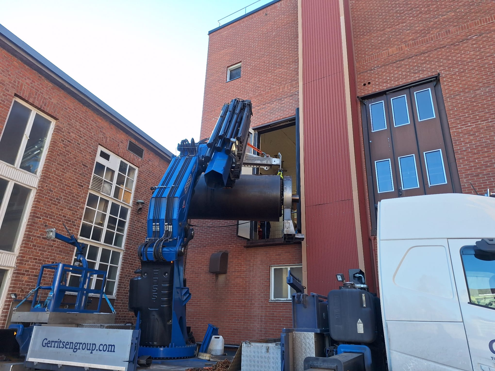 Truck mounted crane of Gerritsen Group lifing part of a machine out of a building through window. 
